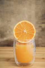 Half orange juicy fruit on a transparent drinking glass isolated on a brown wooden background
