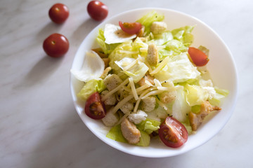 Appetizing and delicious dietary salad consisting of Peking cabbage, tomatoes, cheese, chicken pieces, croutons, located on a light background