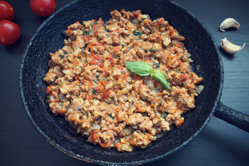 Fried ground meat with vegetables in an old frying pan on a dark background, garlic and tomatoes