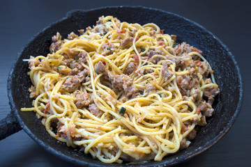 Appetizing spaghetti in an old frying pan with Bolognese sauce on a dark background close up