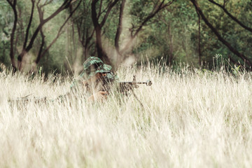 Obraz na płótnie Canvas Soldier hiding in bushes ready to shoot. Ambush his ememy, ready his assault rifle. Hiding below the tree line. Military combat training concept.