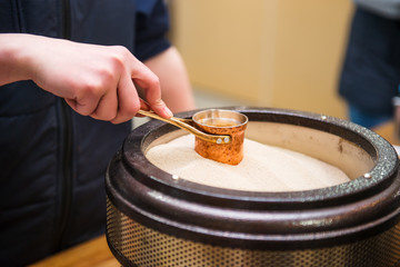 Close up Preparation of Turkish coffee in the cezve in the sand at cafe bar. Professional barista hand cooking coffee in traditional way in modern equipment. Selective focus, space for text.