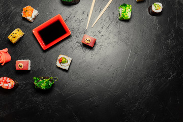 Obraz premium Top view of Japanese Sushi and chopsticks on black background. Sushi rolls, nigiri, maki, pickled ginger, wasabi, soy sauce. Space for text. Top view. Sushi background. food frame