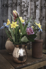 Bouquet of  cut, spring flowers in copper jug standing on garden table.Garden decoration Uk.British spring flowers.