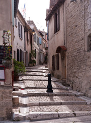 winding, stepped cobblestone street in old area of Arles, France, with American flag above one...