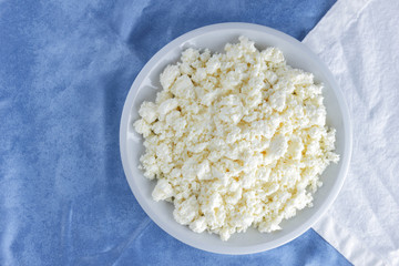 Cottage cheese on a white blue fabric background, soft cheese on a white plate, fresh homemade cheese on a white blue napkin. Dairy product in vintage style, healthy lifestyle. Copy space