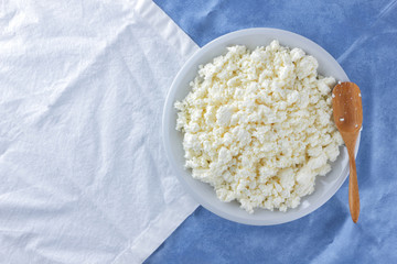 Cottage cheese on a white blue fabric background, soft cheese on a white plate, fresh homemade cheese on a white blue napkin. Dairy product in vintage style, healthy lifestyle. Copy space