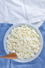 Cottage cheese on a white blue fabric background, soft cheese on a white plate, fresh homemade cheese on a white blue napkin. Dairy product in vintage style, healthy lifestyle. Copy space