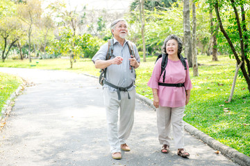 Fototapeta premium Senior couple in park walking with backpack. Chinese old couple in park, relaxing, smiling. With copy space.
