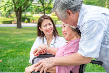 Nurse with senior patient in park. Senior disable woman in wheelchair relaxing and being comfort by a chinese female nurse.