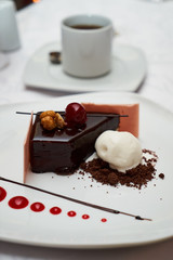 Black forest Cake with cherry, vanilla ice-cream, chocolate and cup of hot tea on table. Delicious sweet dessert breakfast on table background, close-up