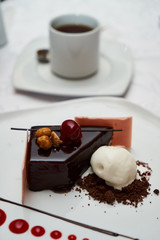 Black forest Cake with cherry, vanilla ice-cream, chocolate and cup of hot tea on table. Delicious sweet dessert breakfast on table background, close-up