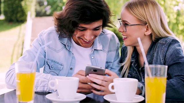 Young couple sitting in cafe's garden and using smartphone for fun