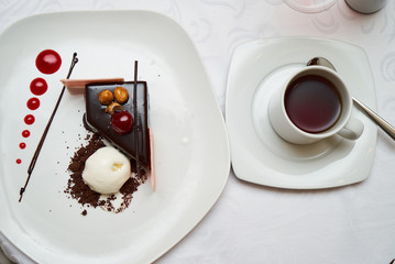Black forest Cake with cherry, vanilla ice-cream, chocolate and cup of hot tea on table. Delicious sweet dessert breakfast on table background, close-up