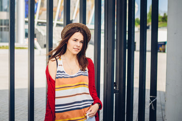 Portrait of a beautiful, stylish young Caucasian woman with a toothy smile, long developing hair in the wind and a straw hat on her head. Dressed in a red sweater and striped blouse