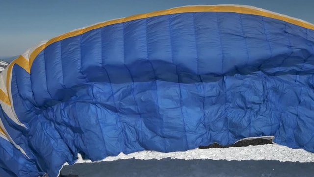 raises the sail wing of the paraglider. He starts to take off, breaks away from the ground, runs away. Paragliding in winter. Slow motion