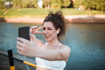 Attractive girl with curly hair taking selfie with her smartphone while exercising outdoors