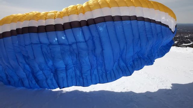 raises the sail wing of the paraglider. He starts to take off, breaks away from the ground, runs away. Paragliding in winter. Slow motion