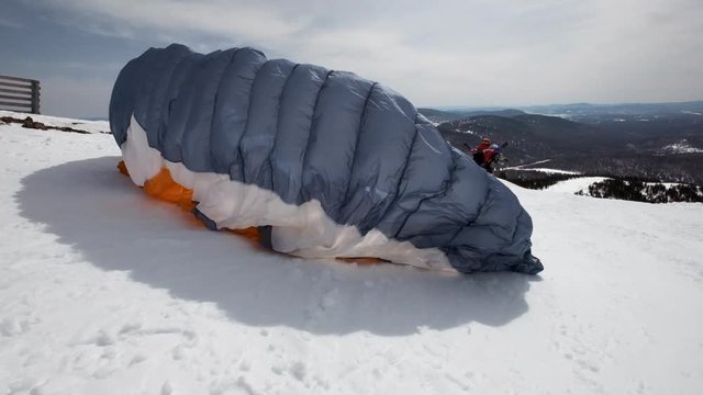 raises the sail wing of the paraglider. He starts to take off, breaks away from the ground, runs away. Paragliding in winter