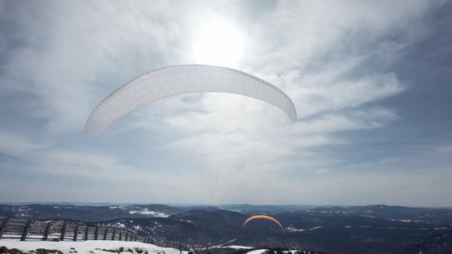 raises the sail wing of the paraglider. He starts to take off, breaks away from the ground, runs away. Paragliding in winter