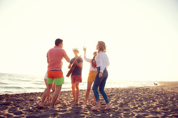 group of happy young people dancing at the beach on beautiful summer sunset