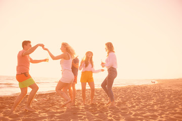 group of happy young people dancing at the beach on beautiful summer sunset