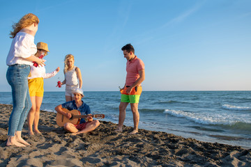 group of happy young people dancing at the beach on beautiful summer sunset