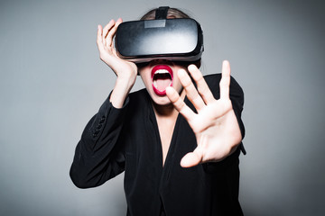 Woman scared in virtual reality glasses. Scared woman using virtual reality goggles on grey background.