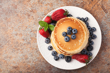 Close-up delicious pancakes, with fresh blueberries, strawberries and maple syrup on a rusty background. With copy space