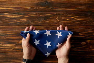 cropped shot of man holding folded american flag on wooden background