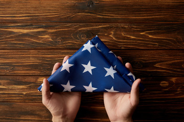 cropped shot of man holding folded united states flag on wooden background