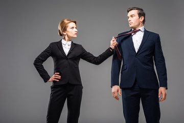 aggressive businesswoman holding tie of businessman, isolated on grey