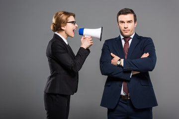 aggressive businesswoman with bullhorn yelling at businessman, isolated on grey, feminism concept