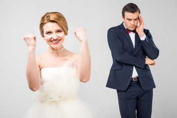 excited bride in wedding dress and worried groom behind, isolated on grey, feminism concept