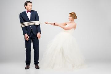 bride bounding groom with rope, isolated on grey, feminism concept