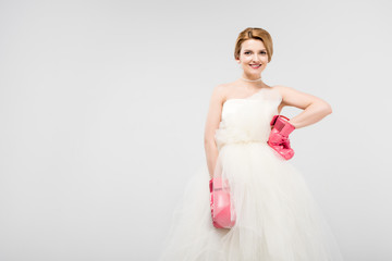 Fototapeta na wymiar beautiful bride posing in wedding dress and boxing gloves, isolated on grey, feminism concept