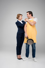 businesswoman and male householder standing together with frying pan, feminism concept, isolated on grey