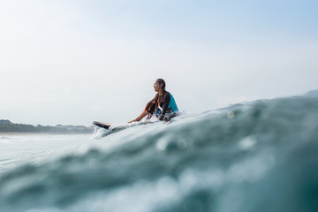 Naklejka premium beautiful young woman sitting on surfboard in ocean