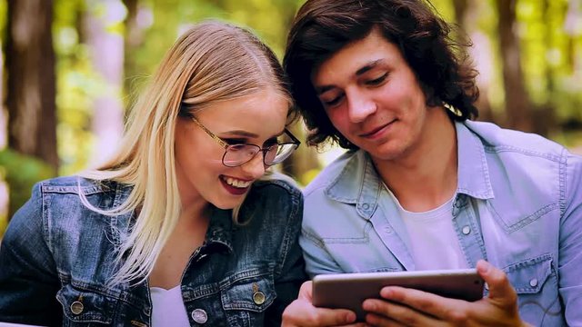 Young Couple Using Tablet While Sitting In Forest