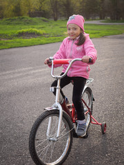 baby girl in pink jacket learning to ride a red bike on the asphalt in the Park
