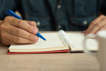 man writing in notebook with pen and coffee cup on wooden table.