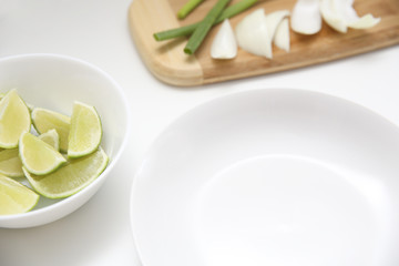 Close up of a white empty dish, chives and sliced onions, sliced limes