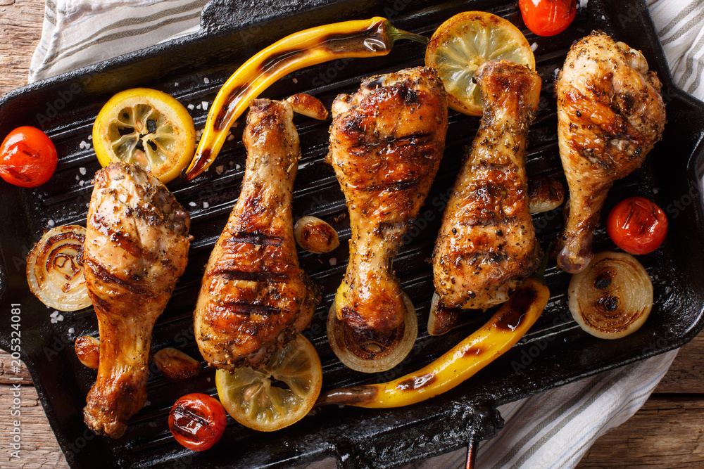 Wall mural delicious food: grilled chicken drumstick legs with vegetables in a grill pan close-up on a table. h