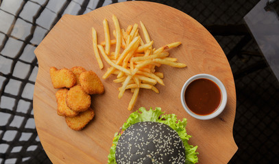 Black burger on a wooden background with potatoes and sauce