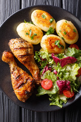 Grilled chicken drumsticks are served with potatoes and fresh salad close-up. Vertical top view