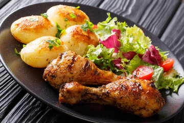 Serving of grilled chicken legs with potatoes and fresh salad closeup on a plate. horizontal