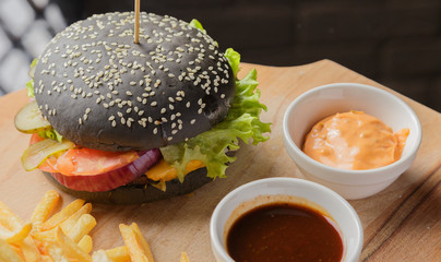 Black burger on a wooden background with potatoes and sauce