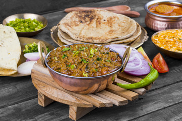 Indian Cuisine Sev Tamatar Also Called Sev Tamaeta or Sev Tameta is Served With Chapati, Papad, Onion or Raita. It is Made With Tomato And Onion Gravy With a Twist of Spicy Sev on Wooden Table
