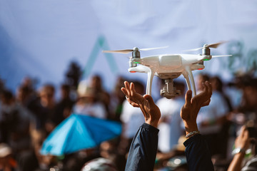 Young operator holding drone above crowd, before working with covering an event