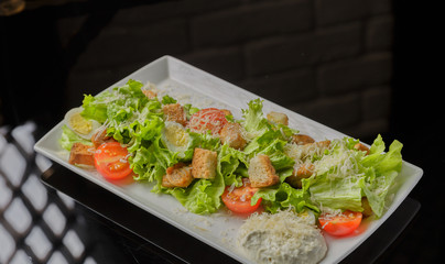 Caesar salad on a white plate and a glass background